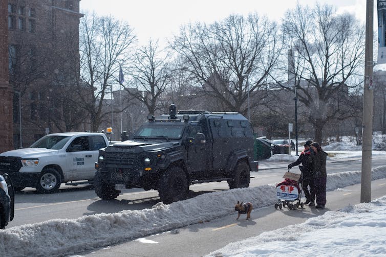 Canadian police are becoming more militarized, and that is damaging public trust 3 A man with dogs walks passed a black military style armoured vehicle on a snowy city street.